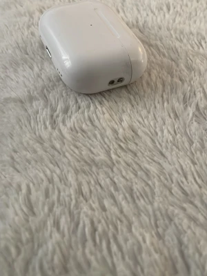 Vita trådlösa hörlurar med laddningsetui - Säljer ett par vita trådlösa hörlurar med matchande laddningsetui. Etuiet är kompakt och har rundade kanter, tillverkat i blank plast. Perfekt för dig som vill lyssna på musik eller poddar utan sladdar.