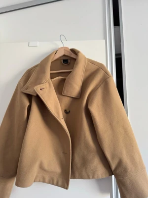 Kort beige ullkappa med krage - Stilren beige kappa i ullmix med bred krage och knäppning framtill. Den är från Gina tricot och har blivit använd men jag har tagit hand om den väl 🩷och nu känner jag att jag vill sälja den då den inte används, nypris (999kr) Köparen står för frakt 