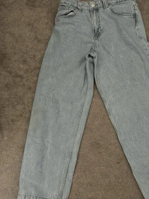 Ljusblå baggy jeans med raka ben - Säljer ett par ljusblå baggy jeans med raka ben och hög midja. Jeansen har klassiska fem fickor, bälteshällor och stängs med knapp och dragkedja. Perfekta för en avslappnad och trendig look. Materialet är denim i bomull.