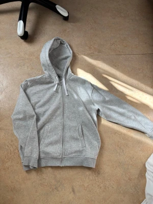 Ljusgrå zip hoodie med huva - En stilren ljusgrå hoodie med dragkedja. Säljer då den ej används. :)