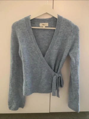 Ljusblå omlottkofta  - Mysig ljusblå stickad omlottkofta från Gina med knytband i midjan och långa ärmar. 