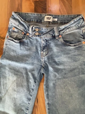 Blå jeans med broderade bakfickor - Snygga blå jeans från 157 med dubbla knappar i midjan och broderade detaljer på bakfickorna. Klassisk femficksmodell i tvättad denim som passar perfekt till en avslappnad stil. Jeansen har normal passform och raka ben.