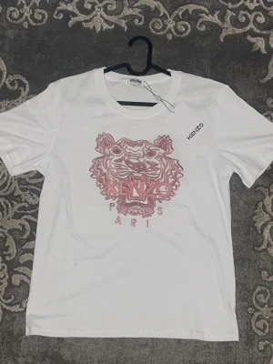 Vit Kenzo t-shirt med tigertryck - Snygg vit t-shirt från Kenzo med ikoniskt tigertryck i rött och texten 'Kenzo Paris' på bröstet. Storlek S men passar M