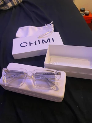 Transparenta solglasögon från CHIMI - Säljer ett par stilrena solglasögon från CHIMI med transparent båge och rektangulär form. Glasögonen har en modern vibe och kommer med originalfodral och förvaringspåse. Perfekta för dig som vill ha en clean och trendig look.