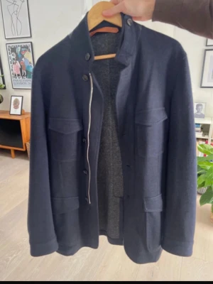 Mörkblå overshirt/m65 från Cortigiani - Stilren mörkblå overshirt från Cortigiani med fyra stora fickor framtill och ståkrage. Tillverkad i wool cotton och lädersom ger en exklusiv känsla. Perfekt lager-på-lager-plagg för dig som gillar en clean och modern look. Jackan går 3000€ i butik. 