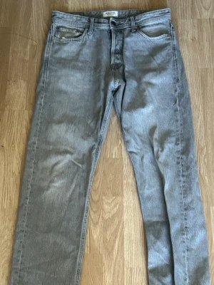 Grå raka jeans från Jack&Jones small Relaxed/Chris fit - Snygga grå jeans från Asos med rak passform och klassisk femficksdesign. Jeansen har en ljusgrå tvätt och är tillverkade i denim med normal midja. Perfekta för en avslappnad och trendig stil.