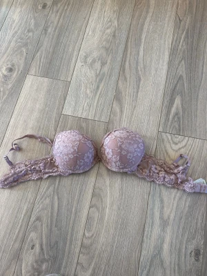 Rosa spets-bh med blommönster - Söt bh i en blandning av ros och syrenlila med vadderade kupor och vacker spets med blommönster. Axelbanden är justerbara och bh:n har hakknäppning bak. Perfekt för dig som gillar romantiska detaljer och mjuka färger.