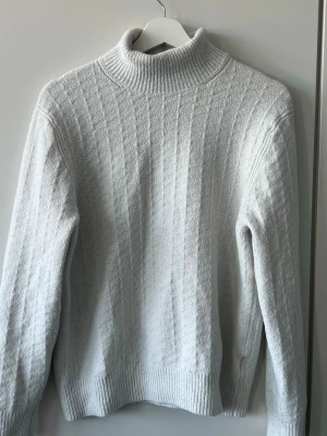 Vit stickad polotröja - Säljer en stilren vit stickad polotröja med ribbad hög krage och diskret rutmönster i strukturen. 