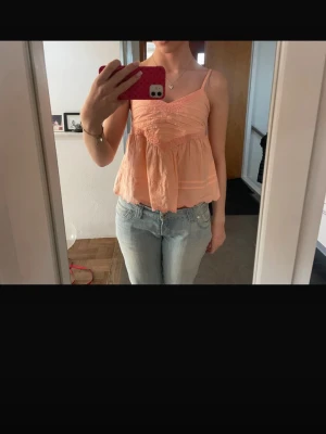 Persikofärgad volangtop med smala band - Söt persikofärgad topp med tunna axelband och volang nedtill. Säljer pågrund av att den inte kommer till användning .