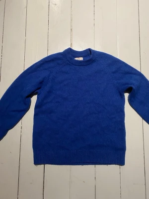 Blå stickad tröja från Rugged Goods - Säljer en blå stickad tröja från Yoke, Rugged Goods i ullblandning. Tröjan har rund halsringning, långa ärmar och ribbade muddar vid ärmslut och nederkant. Enkel och stilren design som passar perfekt till kalla dagar.