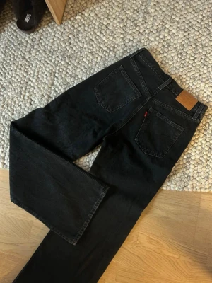 Svarta Levi's wide leg jeans w26 L32 - Säljer ett par grå/svarta Levi's jeans med breda ben och hög midja. Klassisk femficksmodell i kraftig denim med snygga detaljer som nitar och läderpatch bak. Perfekta för en avslappnad och trendig look.