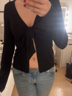 Svart långärmad topp med knyt framtill - Säljer en svart topp med lång ärm och v-ringning. Använde 2-3 gånger för ett tag sedan men känner att den behöver en nu ägare nu då den bara ligger i garderoben