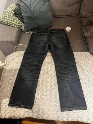 Mörkblå raka jeans med kontrastsömmar - Säljer ett par mörkblå jeans med raka ben och snygga kontrastsömmar. Jeansen har klassisk femficksdesign och är tillverkade i kraftig denim. Perfekta för en avslappnad och stilren look.