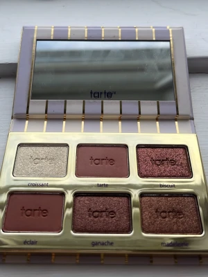 Tarte ögonskuggspalett med spegel - Snygg ögonskuggspalett från Tarte med sex nyanser i både matta och skimrande toner. Färgerna går i beige, brunt, koppar och guld. Paletten har en lyxig design med guldiga detaljer och inbyggd spegel, perfekt för att skapa olika ögonlooks.💗👍