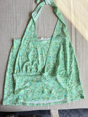 Grönt blommigt set halterneck med kjol - Söt grön halterneck linnetopp och kjol från Nelly med blommigt mönster i pastellfärger. Toppen har knyt i nacken och djup v-ringning framtill. Perfekt för varma dagar och ger en fräsch sommarkänsla. Oanvänt 💚