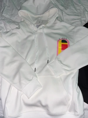 Vit hoodie från Casablanca - Säljer en vit hoodie från Casablanca (lapp fof på) med färgglatt grafiskt tryck i rosa, gult, rött och svart på både bröstet och ryggen. Hoodien har huva med dragsko, magficka och ribbade muddar. Perfekt för dig som gillar streetwear och unika prints. 