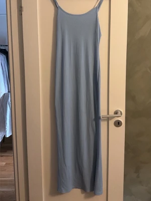 Ljusblå långklänning med tunna band - En enkel och stilren ljusblå långklänning med tunna axelband och rak passform. Klänningen har en minimalistisk design och är perfekt för varma dagar. Materialet känns mjukt och svalt mot huden.