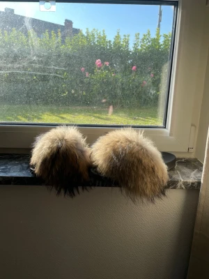 Tofflor med fluffig fuskpäls - Säljer ett par trendiga tofflor med stor, fluffig fuskpäls i beige, brunt och svart. Tofflorna har en klassisk slip-in modell med svart sula och ger en riktigt lyxig känsla. Perfekta för dig som vill ha något extra till vardagslooken.