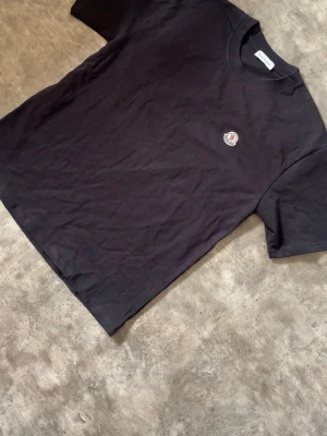 Svart Moncler t-shirt med logga - Snygg svart t-shirt från Moncler med klassisk rund hals och liten broderad logga på bröstet. Enkel och stilren design som passar till det mesta. Tillverkad i mjuk bomull för en skön känsla.