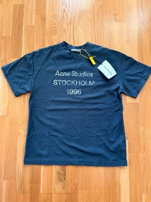 Acne Studios t-shirt - Snygg mörkblå t-shirt från Acne Studios med tryck 'STOCKHOLM 1996' på bröstet. Klassisk passform och korta ärmar. Tillverkad i mjuk bomull, perfekt för en clean och stilren look.
