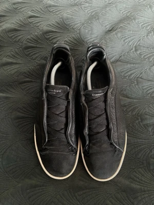 Svarta sneakers från Ermenegildo Zegna - Stilrena svarta sneakers från Ermenegildo Zegna med ovandel i slätt och strukturerat läder. Skorna har svarta snören och vit sula som ger en snygg kontrast. Perfekta för dig som gillar minimalistisk och exklusiv design. Hållen går ej igenom 