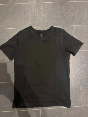 Svart v-ringad t-shirt från H&M - En svart basic t-shirt från H&M i ekologisk bomull. T-shirten har v-ringning och korta ärmar, perfekt för en enkel och stilren look. Passar dig som gillar klassiska plagg med en clean vibe.