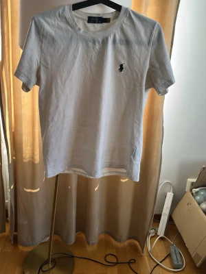 Vit t-shirt från Polo Ralph Lauren - Klassisk vit t-shirt från Polo Ralph Lauren med rund halsringning och den ikoniska svarta logotypen broderad på bröstet. Tillverkad i mjuk bomull och har en normal passform med korta ärmar. Perfekt basplagg till garderoben. Finns dock lite märkningar  längst ner på framsidan av T-shirten därför priswr