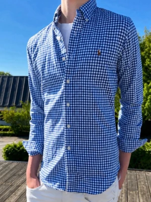 Blårutig skjorta med knappar - Snygg blårutig skjorta med klassisk button-down krage och vita knappar. Skjortan har lång ärm och är tillverkad i ett mjukt bomullstyg. Perfekt för dig som gillar en stilren och avslappnad look.