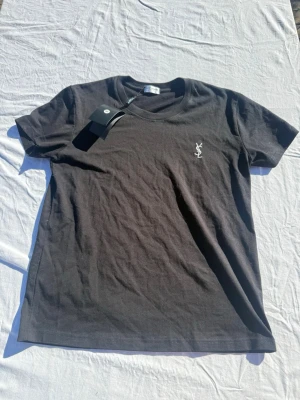 Svart t-shirt från Saint Laurent - Snygg svart t-shirt från Saint Laurent med klassisk rund hals och vit YSL-logga broderad på bröstet. Tröjan är storlek M men passformen är nog lite mer åt S hållet. Tveka inte att skriva vid fundering eller för fler bilder//Felkannn