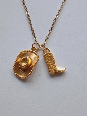 Guldigt halsband med cowboyhatt och cowboy boots 🤠 - Unikt halsband i guldigt rostfritt stål metall med två hängen: en detaljerad cowboyhatt och en westernstövel. Kedjan är tunn och elegant, och båda berlockerna har fina mönster som ger en cool western-vibe yeehaaa 🤠 materialet rostfritt stål.