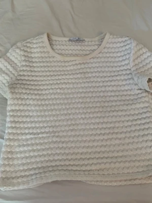 Vit strukturerad kortärmad topp - Säljer en vit topp med korta ärmar och rund hals. Toppen har en strukturerad, vågig yta som ger en unik look. Perfekt till jeans eller kjol för en fräsch och enkel stil. Materialet känns mjukt och luftigt, vilket gör den skön att bära under varmare dagar. Storlek xs