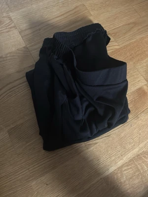 Svarta mjukisbyxor  - Säljer ett par svarta mjukisbyxor med resår i midjan och dragsko för skön passform. Byxorna är i mjukt material och har en avslappnad passform, perfekta för chill dagar. Passar dig som gillar enkel och stilren look.