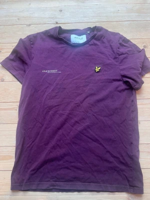 Vinröd t-shirt från Lyle & Scott - Snygg vinröd t-shirt från Lyle & Scott. T-shirten har rund hals och korta ärmar, perfekt för en avslappnad stil. 