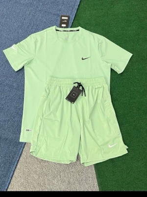 Nike ljusgrönt träningsset - Säljer ett fräscht ljusgrönt träningsset från Nike med t-shirt och shorts. Setet har en stilren design med Nike-logga på både tröja och shorts. Materialet är lätt och andas, perfekt för träning eller sportaktiviteter. Shortsen har dragsko i midjan och praktiska fickor.