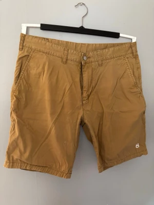 Beiga shorts från 8848 Altitude - Snygga beiga shorts från 8848 Altitude med klassisk passform. Shortsen har bälteshällor, sidofickor och två bakfickor med knapp. Perfekta för varma dagar och enkla att matcha med olika stilar.
