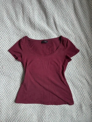 Vinröd t-shirt med rund hals - En enkel och stilren vinröd t-shirt med rund halsringning och korta ärmar. Modellen är figurnära och passar perfekt till jeans eller kjol. Tillverkad i mjuk bomull för en bekväm känsla hela dagen.