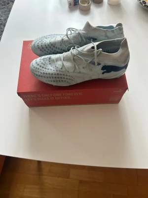 Ljusblå Puma fotbollsskor strl 44 - Säljer ett par ljusblå fotbollsskor från Puma med svart logga på sidan. Skorna har en modern, strömlinjeformad design med mönstrad ovandel och snörning. Perfekta för dig som vill ha bra grepp och stil på planen. Använda 1 vecka under en cup och säljer nu för har inget behov. Inget slitage utan vissa tecken av uteanvändning med klister (handboll). Går lätt bort för den som har tiden