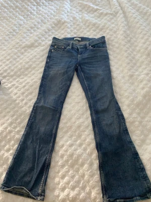 Blå bootcut jeans med broderade fickor - Snygga blå bootcut jeans med klassisk femficksdesign och broderade detaljer på bakfickorna. Jeansen har låg midja och är tillverkade i denim med lätt tvättad look. Perfekta för dig som gillar en avslappnad men trendig stil.