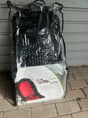 Babysitter 2me Lotta svart/röd - Babysitter Lotta från 2me i svart och röd färg. Sitsen är vadderad och har säkerhetsbälte samt metallram. Kommer i praktisk genomskinlig förvaringsväska med dragkedja och handtag. Perfekt för småbarn och enkel att ta med.