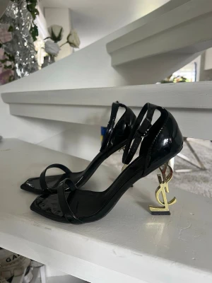 Svarta klackarskor  - Snygga svarta pumps.  i lackat läder med öppen tå och tunna remmar. Klacken är i guld, vilket ger en lyxig och unik look. Perfekta för dig som vill sticka ut och älskar night outs with the girls. Bekväma att gå i 