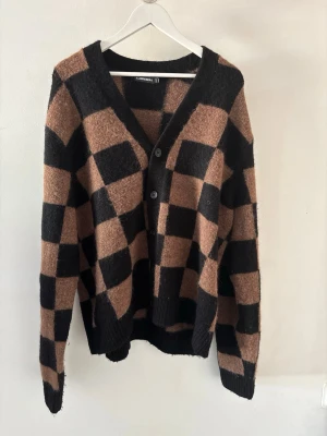 J Lindeberg Cardigan - Säljer en J Lindeberg Cardigan med schackrutigt mönster i brunt och svart. Koftan har v-ringning, knäppning framtill med tre knappar och ribbade muddar vid ärmslut och nederkant. Perfekt för dig som gillar statement-plagg och en avslappnad stil. Nypris 2800, nuvarande pris går att diskutera vid smidig affär.