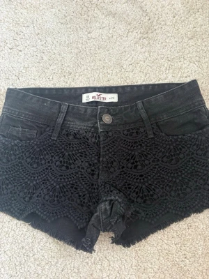 Svarta spetsdetaljerade shorts Hollister - Säljer ett par svarta shorts från Hollister med snygga spetsdetaljer framtill och råa kanter. Klassisk femficksmodell med knapp och dragkedja. Perfekta för sommaren och ger en cool vibe till din outfit.💓