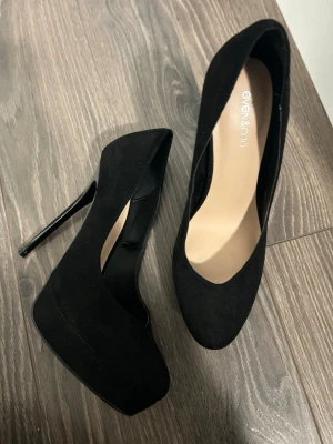 Svarta pumps från Even&Odd - Snygga svarta pumps från Even&Odd med hög klack och platåsula. Skorna har en klassisk rundad tå och är tillverkade i mockaimitation. De är i storlek 39.