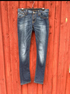 Mörkblå slim fit jeans - Snygga mörkblå slim fit jeans med slitningar och kontrastsömmar. Klassisk femficksmodell med gulddetaljer på bakfickorna och knappgylf. Jeansen har en tvättad look och smal passform som ger en modern stil. Storlek 30/32. Sitter slim. Bara att höra av sig vid frågor/funderingar.