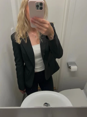 Svart kavaj - Snygg svart kavaj med diskreta smala vita ränder och klassisk krage. Kavajen har en knapp framtill och två fickor med lock. Perfekt för en stilren och trendig look. Fodrad insida och figurnära passform. Sitter som storlek S.