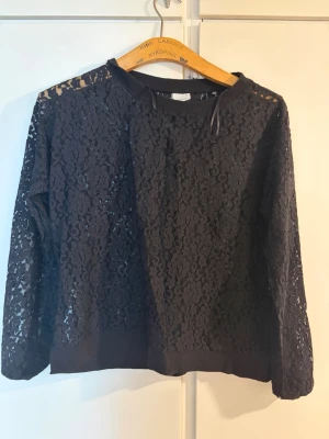 Svart spetsig tröja från Gina Tricot - Säljer en svart långärmad tröja från Gina Tricot i genombruten spets. Tröjan har rund halsringning, ribbade muddar och ett snyggt blommigt spetsmönster som ger en trendig look. Perfekt för dig som gillar detaljer och vill sticka ut. Helt ny aldrig använd!!!