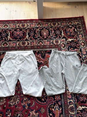 Vita mjukisbyxor med dragsko - Säljer ett par vita mjukisbyxor med dragsko i midjan och fickor på sidorna. Byxorna har en avslappnad passform och ett litet broderat logomärke på vänster sida. Perfekta för chill dagar eller när du vill vara bekväm.