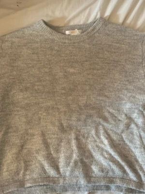 Grå stickad tröja från Gina Tricot - Mysig grå stickad tröja från Gina Tricot med rund halsringning och ribbade muddar. Perfekt för lager på lager och enkel att matcha med olika outfits. Klassisk modell som passar till allt.