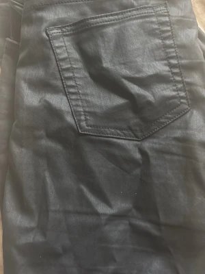 Svarta skinnbyxor  med bakficka - Snygga svarta skinny jeans med klassisk bakficka och stilren design. Jeansen har en lätt glansig finish och är perfekta för dig som gillar en modern och enkel look. Materialet känns mjukt och följsamt.
