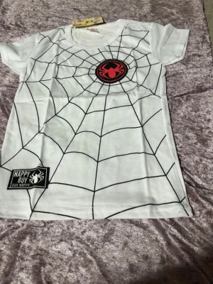Vit  spindelman T shirt  - Vit t-shirt med svart spindelnätsmönster och en röd spindel-logga på bröstet. Rund halsringning och korta ärmar. Perfekt för dig som gillar coola och unika tryck. Finns Stlk kvar 100,110,120 